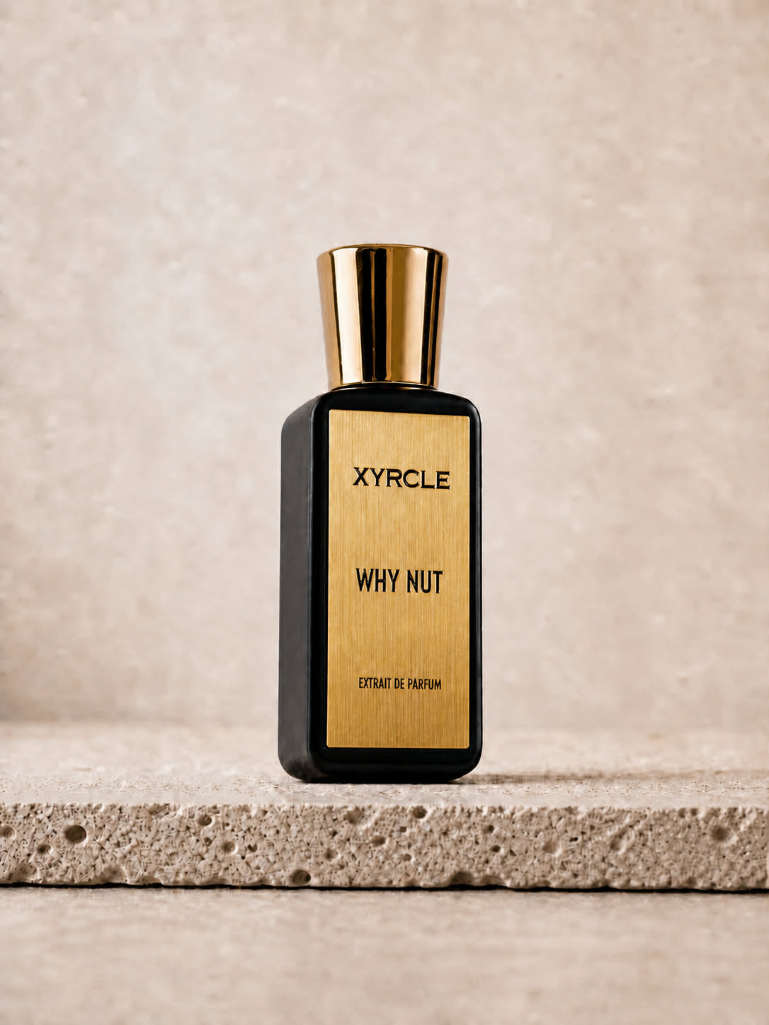 Elegant black and gold perfume bottle labeled "XYRCLE WHY NUT" stands on a textured stone surface