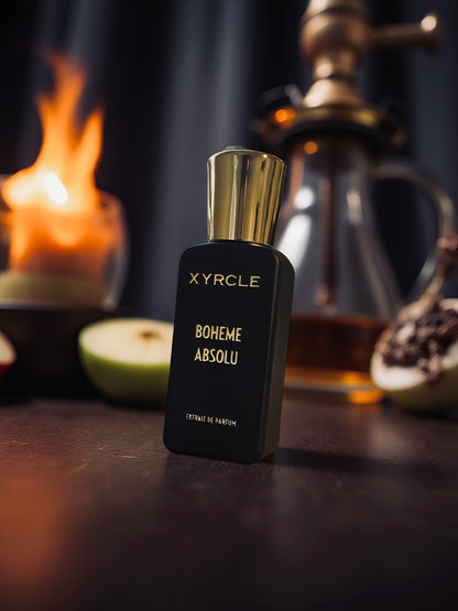 Perfume bottle labeled "XYRCLE Boheme Absolu" with a gold cap on a table. A lit candle, sliced apple, and glass decanter in the blurred background.